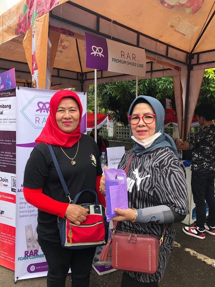 Dua pelanggan berfoto di depan banner RAR Premium Shoescare sambil memegang produk